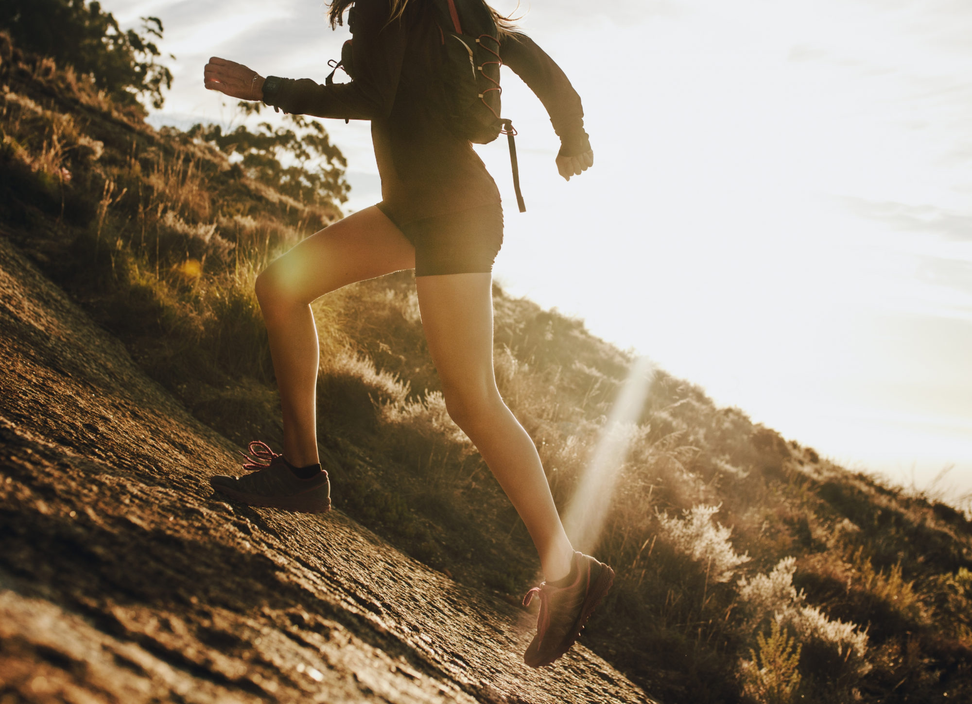 Woman running up a rocky mountain slope. Cropped shot of female trail runner running uphill on a sunny day.